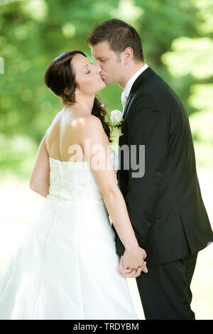 Wedding picture of a bridal couple holding hands and kissing outdoors Stock Photo