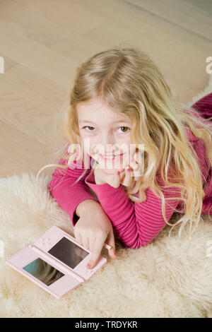 Portrait of a girl lying on the floor and playing with her Nintendo console Stock Photo