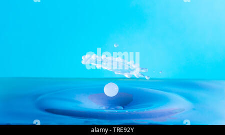 water drop falling and impacting a body of water after hitting the surface and forming different water droplets on a blue background. Stock Photo