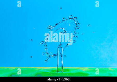 water drop falling and impacting a body of water after hitting the surface and forming different water droplets on a blue background. Stock Photo
