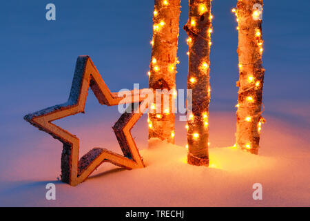 wooden star and illuminated birch trunks in snow, Switzerland Stock Photo