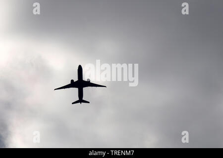 Airplane flying on storm clouds background. Silhouette of a passenger plane in the dark dramatic sky Stock Photo