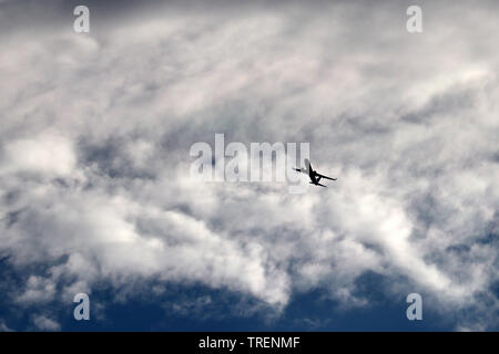 Airplane flying in the sky on background of clouds. Silhouette of a commercial plane during the turn Stock Photo