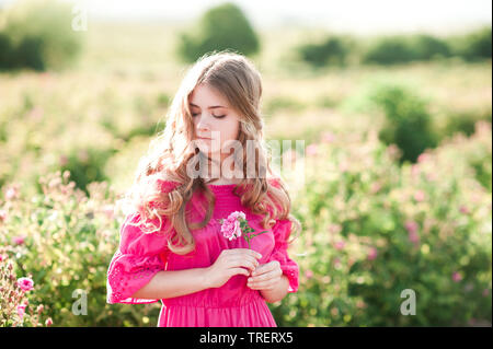 Beautiful blonde teen girl 14-16 year old wearing pink dress holding rose  flower outdoors. Summer portrait Stock Photo - Alamy