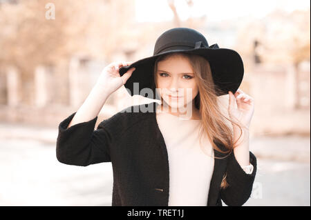 Smiling teenage girl wearing black hat and winter coat outdoors. Looking at camera. Teenager hood. Autumn portrait. Stock Photo