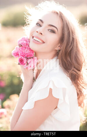 Smiling blonde girl 24-29 year old holding roses outdoors. Looking at camera. 20s. Summer season. Stock Photo