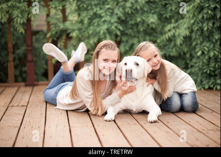 Happy girls having fun with pet labrador outdoors. Lying on wooden floor. Looking at camera. Happiness. Togetherness. Stock Photo