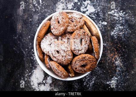 Fresh baked chocolate chip and oat fresh cookies with sugar powder heap in white bowl on black background. Top view. Stock Photo