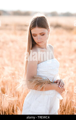 Beautiful blonde girl 14-16 year old holding wheat in field. Summer season. 20s. Stock Photo