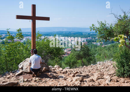 Medjugorje, Bosnia and Herzegovina - July 6 2012: A pillgrim kneeling and praying in front of wooden cross in famous pilgrimage place Apparition hill, Stock Photo