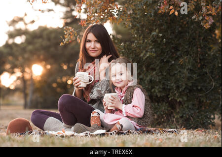 Smiling kid girl sitting with mother drinking hot tea in park. Looking at camera. Motherhood. Stock Photo