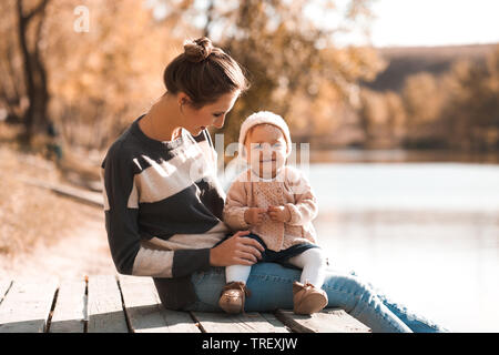 Young mother playing with her toddler daughter outdoors in park. Wearing knitted sweaters. Family time. Stock Photo