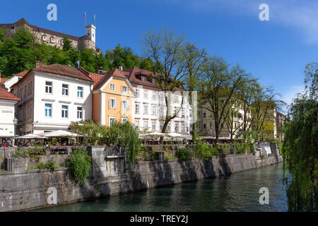 Old tenements and medieval castle on hill above historical center of capital city of Ljubljana, Slovenia. Tourists walking and relaxing at river bank Stock Photo