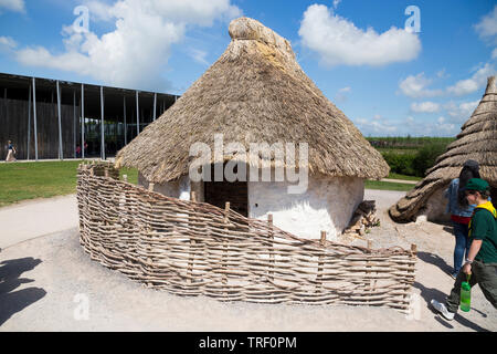Exterior of recreated Neolithic stone age hut / stoneage huts with thatched roof / roofs whilst tourists walk around. Village exhibition; Visitor centre Stonehenge / Stone Henge. Amesbury, Wiltshire, UK (109) Stock Photo