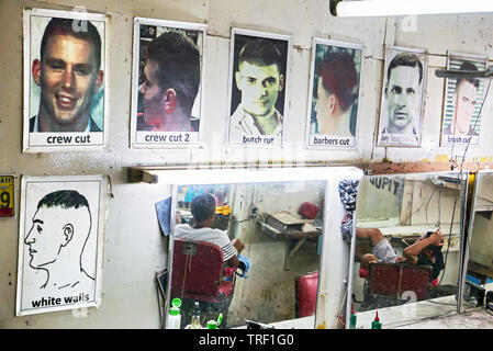 Puerto Princesa City, Palawan, Philippines: Pictures of sample hair cuts and mirrors hanging at a wall in an old barber shop Stock Photo