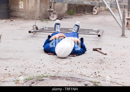 Workplace accident on a construction site. A worker wearing helmet and protective workwear lying injured on the site Stock Photo