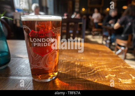 A pint of Fuller's London Pride beer on a wooden tabletop in a pub Stock Photo
