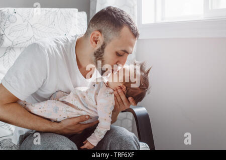 Caucasian father sitting in armchair with newborn baby girl. Parent holding kissing child daughter son on his hands. Authentic lifestyle documentary m Stock Photo