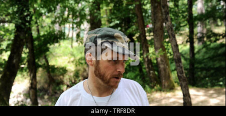 Outdoors horizontal portrait of happy hiker young man with red beard, feel good after hiking in forest. Traveler bearded male smiling and feel happy d Stock Photo