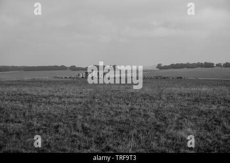 A black and white photo shows an overview of tourists, in the distance, admiring the famous prehistorical monument of Stonehenge in Wiltshire. Stock Photo