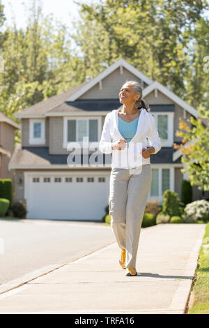 Happy, middle-aged black African American woman running exercising in suburban neighborhood. Active, healthy mature lifestyles. Stock Photo