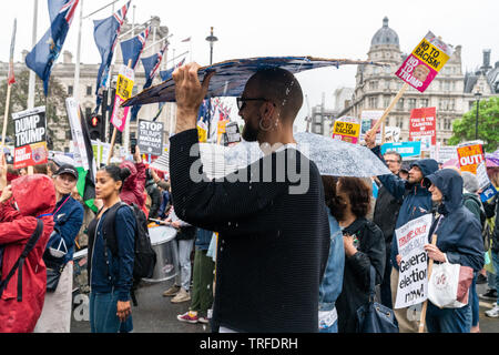 4th June 2019. London, UK. Anti Trump rally in Westminster. A protestor hides from rain under the placard. Stock Photo