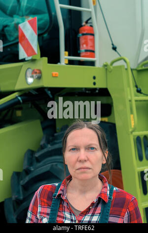 Female farmer posing in front of combine harvester. Serious woman farm worker with agricultural machinery ready harvest crops. Stock Photo