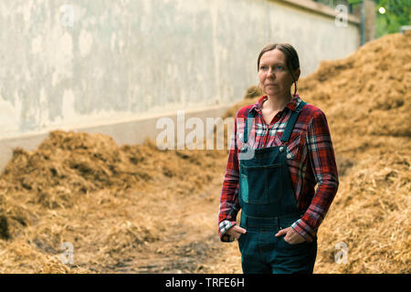 Female farmer standing in front of the horse manure pile on the livestock farm Stock Photo