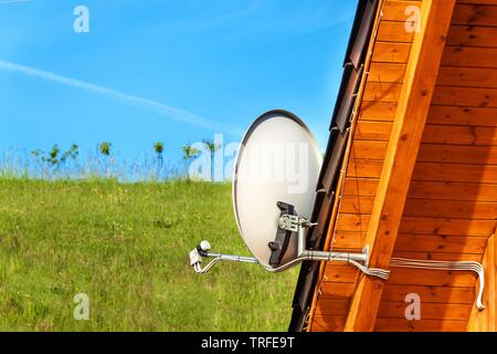 Satellite TV antenna on a wooden house. TV signal transmission. Internet Access. Telecommunication means. Stock Photo