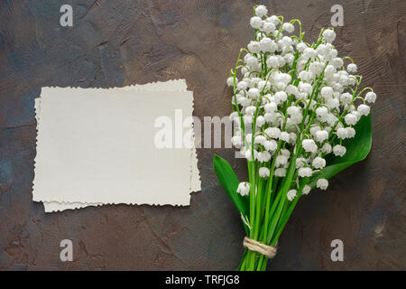 Retro empty photo frame for the inside and Lilies of the valley bouquet on dark brown background. Top view. Stock Photo