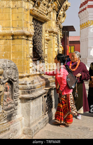 Women in traditional dress worshipping at a gilded niche of the large stupa at Swayambhunath Buddhist temple, Kathmandu, Kathmandu Valley, Nepal Stock Photo