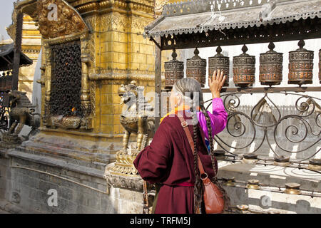 Tibetan woman in traditional dress spinning prayer wheels at a gilded niche of the large stupa at Swayambhunath Buddhist temple, Kathmandu, Kathmandu Stock Photo