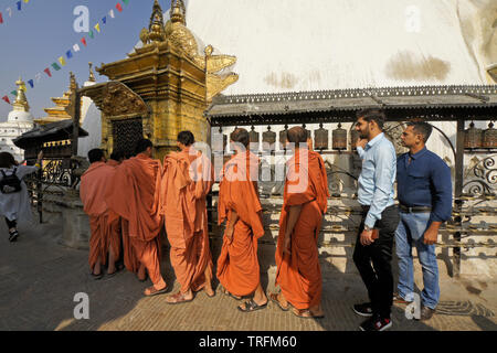 Buddhist monks in orange robes and other visitors spinning prayer wheels at a gilded niche of the large stupa at Swayambhunath Buddhist temple, Kathma Stock Photo