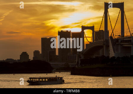A yakatabune pleasure boat in Tokyo Bay at sunset in front of Rainbow Bridge, Odaiba, Tokyo, Japan. Thursday May 30th 2019