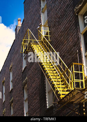 Yellow fire escape on the side of a old brick building with blue sky in background Stock Photo