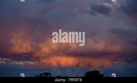 Amazing nature, sky, dramatic backlit heavenly pink, orange and blue clouds at sunset, sunlight shining through on them, ominous from below Stock Photo