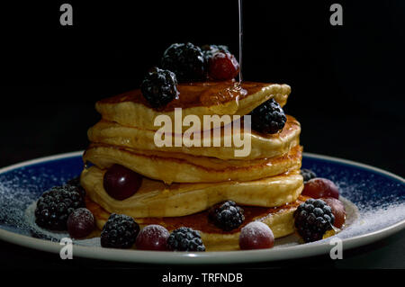 Stacked pancakes with summer berries and dripping honey maple syrup, isolated on black. Food, breakfast,snack. Copy space Stock Photo