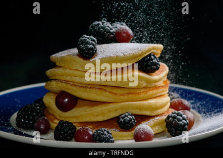 Stacked pancakes with summer berries and falling confectioners sugar , isolated on black. Stock Photo