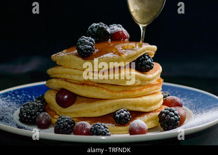 Stacked pancakes with summer berries and falling honey syrup, isolated on black. Food, breakfast,snack. Copy space Stock Photo