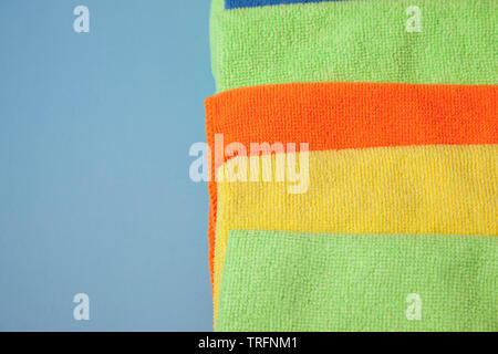 Green, blue, yellow and orange cleaning cloths or facecloths ready for use against a blue background with negative space Stock Photo