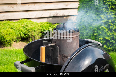 Smoking charcoal briquettes in a chimney starter prepared for a garden barbecue party. Stock Photo