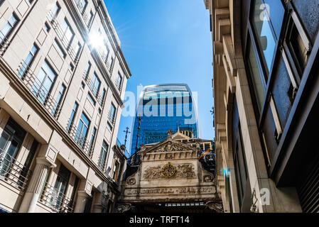 London, UK - May 14, 2019:  Low angle view of the entrance to Leadenhall Market and The Gherkin skyscraper in the City of London against blue sky.