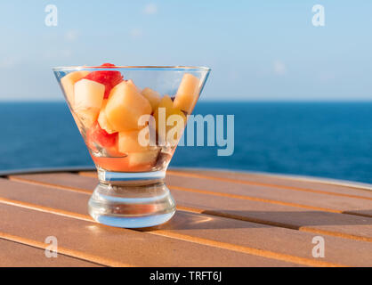 Fresh mixed fruit salad on wooden table. Blurred ocean background. Stock Photo