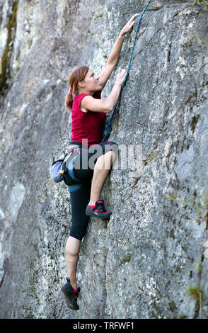 Climber in red t-shirt climbs a gray rock. A strong hand grabbed