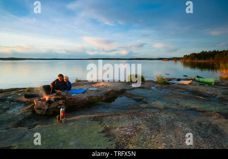 Father and son beside the bonfire at the island Brattholmen in the lake Vansjø in Østfold, Norway. Vansjø is the largest lake in Østfold. The lake Vansjø and its surrounding lakes and rivers are a part of the water system called Morsavassdraget. September, 2006. Stock Photo