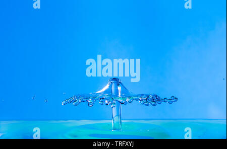 water drop falling and impacting a body of water after hitting the surface and forming different water droplets on a blue background. Stock Photo