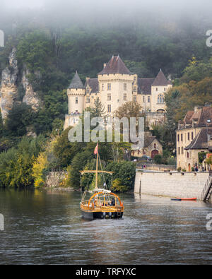 A traditional boat sails along the Dordogne River in front of the village of La Roque-Gageac in the Perigord region of France Stock Photo
