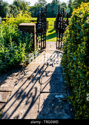Shadows on a stone path leading to a gate into an English country garden in Derbyshire UK Stock Photo