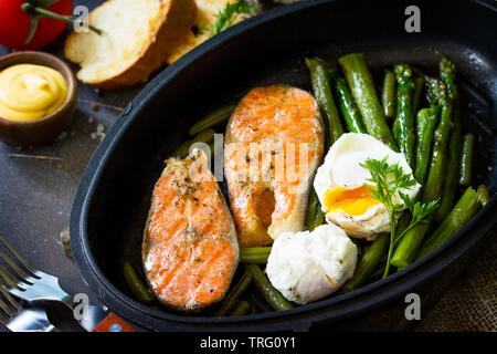 Salmon fish steak grilled with asparagus, poached egg in a frying pan on a rustic stone table. Healthy food. Stock Photo