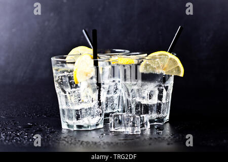 Three glasses of fresh cold carbonated water with ice cubes and lemon slices. Soda water on black background. Stock Photo